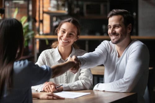 Smiling couple shakes hands with a real estate agent, signifying a successful negotiation and agreement in a positive, professional environment.